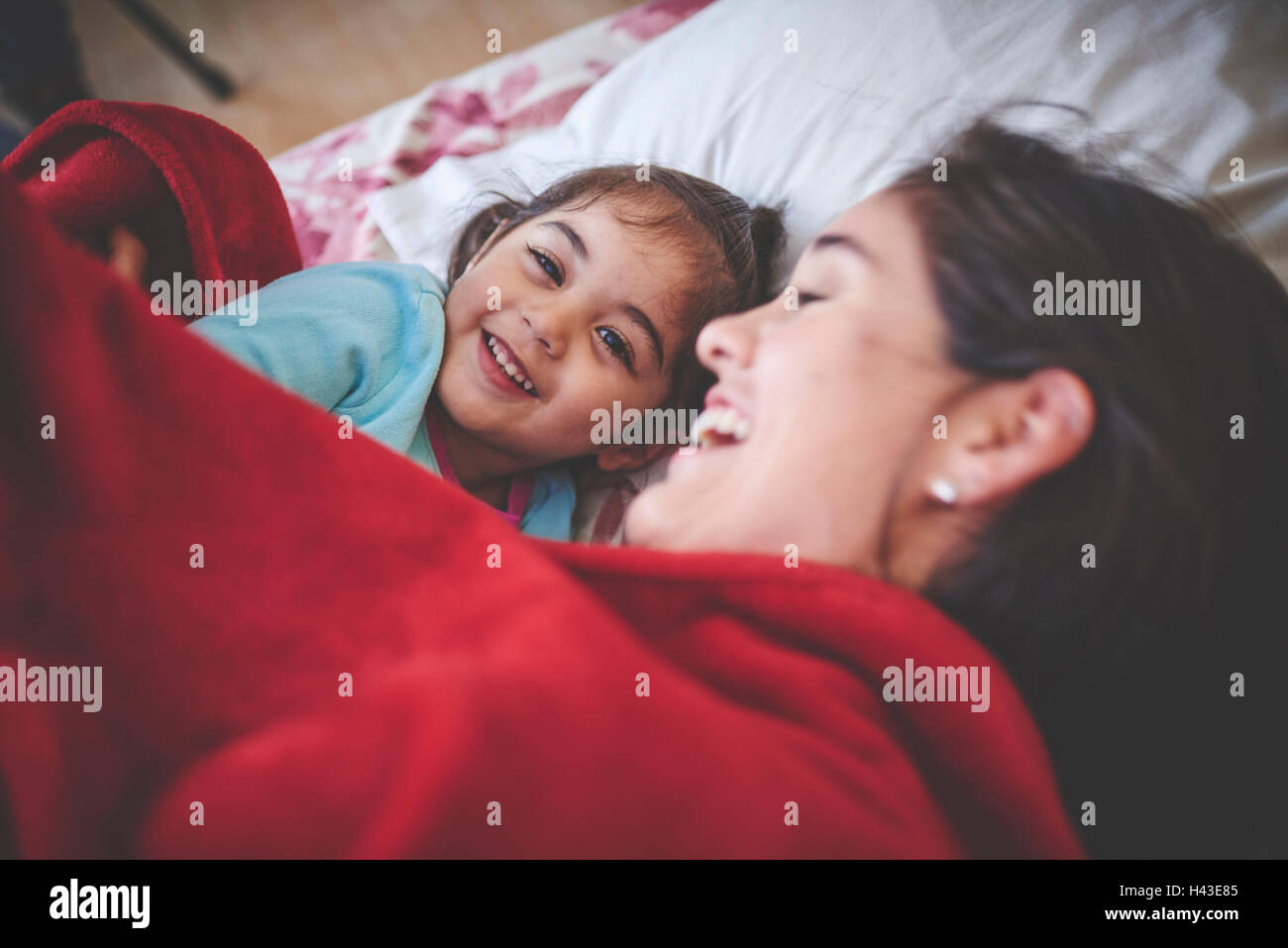 Lachen, Hispanic Mutter und Tochter unter roter Decke im Bett Stockfoto
