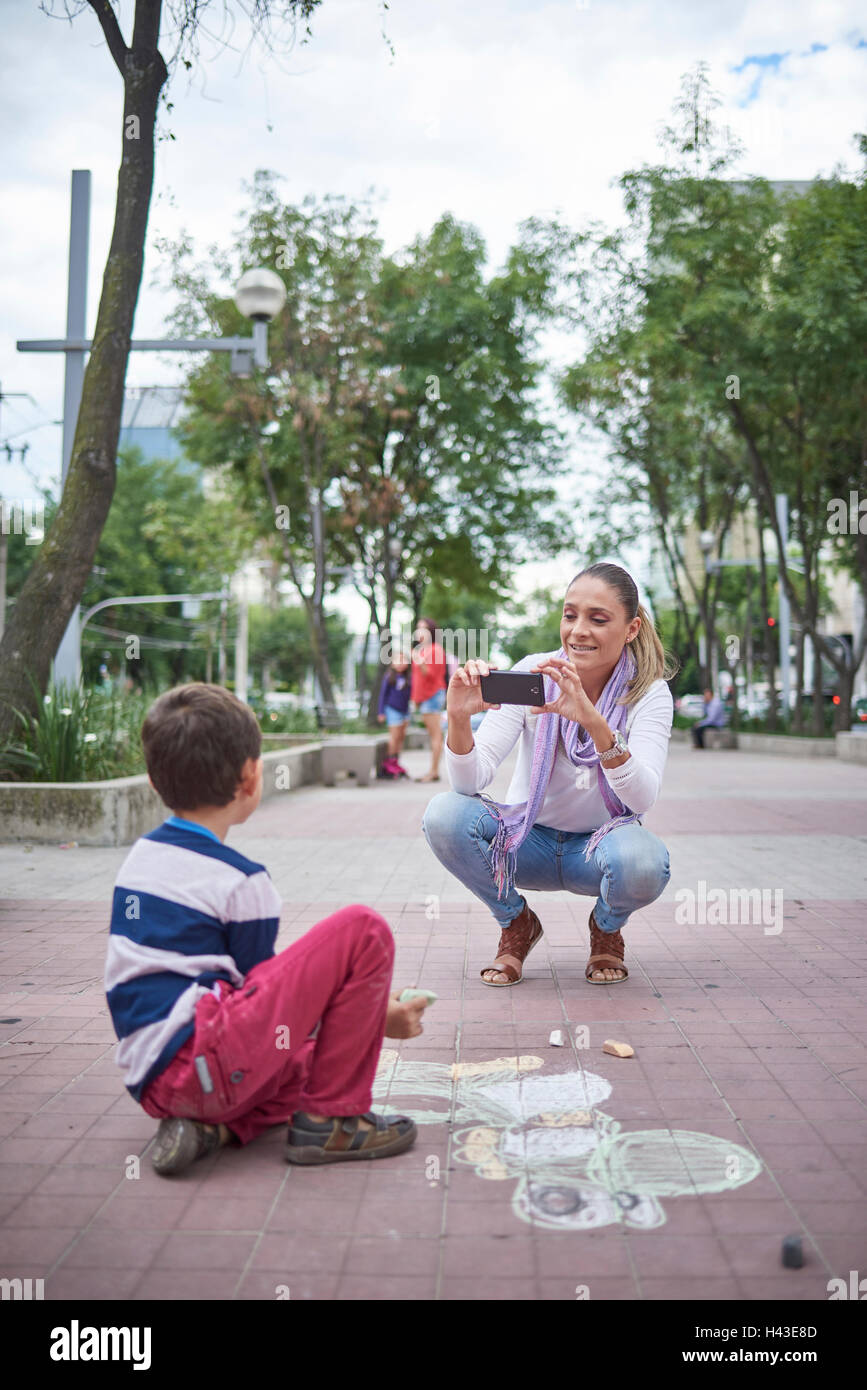 Hispanische Mutter fotografieren Sohn auf Bürgersteig Stockfoto