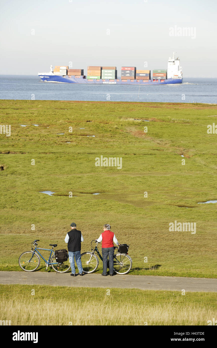 Deutschland, Niedersachsen, Cuxhaven, Küste, Salzwiesen, Radfahrer, Ruhe, Meerblick, Containerschiff, Norddeutschland, Nordsee, Küste, Nordseeküste, Meer, Schiff, Frachter, Frachtschiff, Strand, Person, älteres Paar, Senioren, Fahrräder, Freizeit, Ausflüge, Radfahren, Tour, Aktivität, Gesundheit, Urlaub, Freizeit, Stockfoto