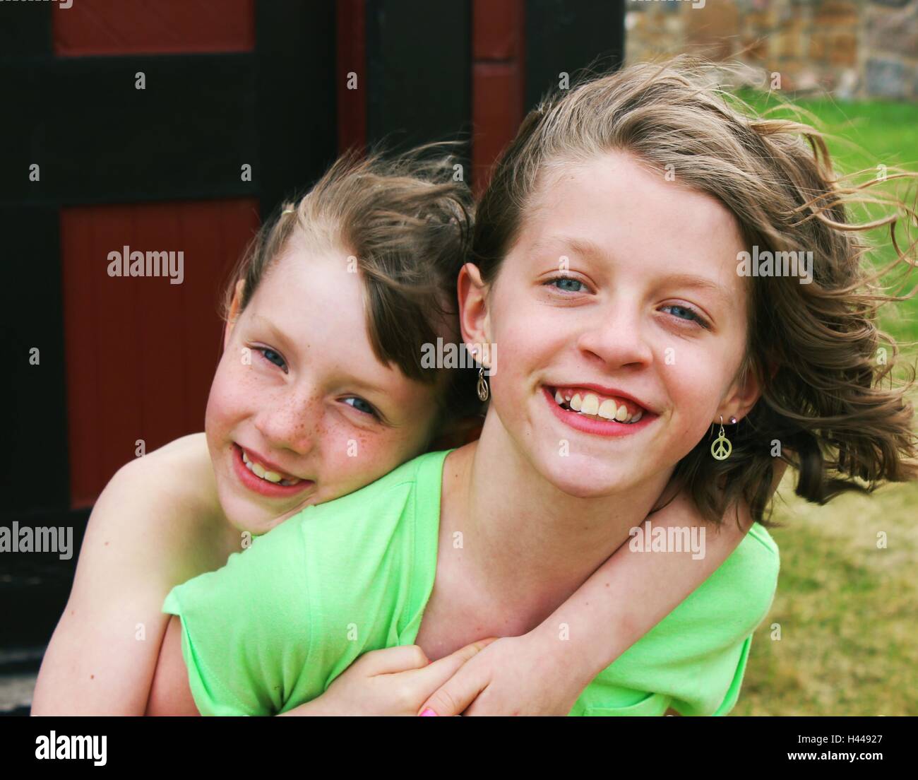 Zwei glückliche junge Mädchen oder Geschwister, Schwestern für die Kamera posieren, Huckepack Fahrt Stockfoto