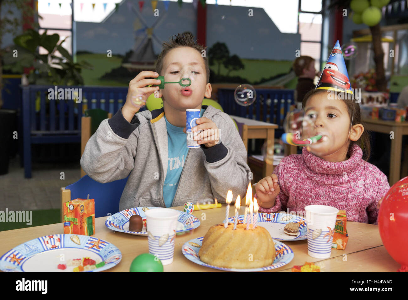 Kinder Geburtstagsparty, junge, Mädchen, Papierhüte, Seifenblasen, Kuchen, Kerzen, brennen, Menschen, Kinder, Geschwister, Geburtstagstorten, Party, Geburtstagsparty, feiern, Vergnügungen, glücklich, spielen, Party-Mützen, Kopfbedeckungen, Spaß, Freude, fröhlich, Stockfoto