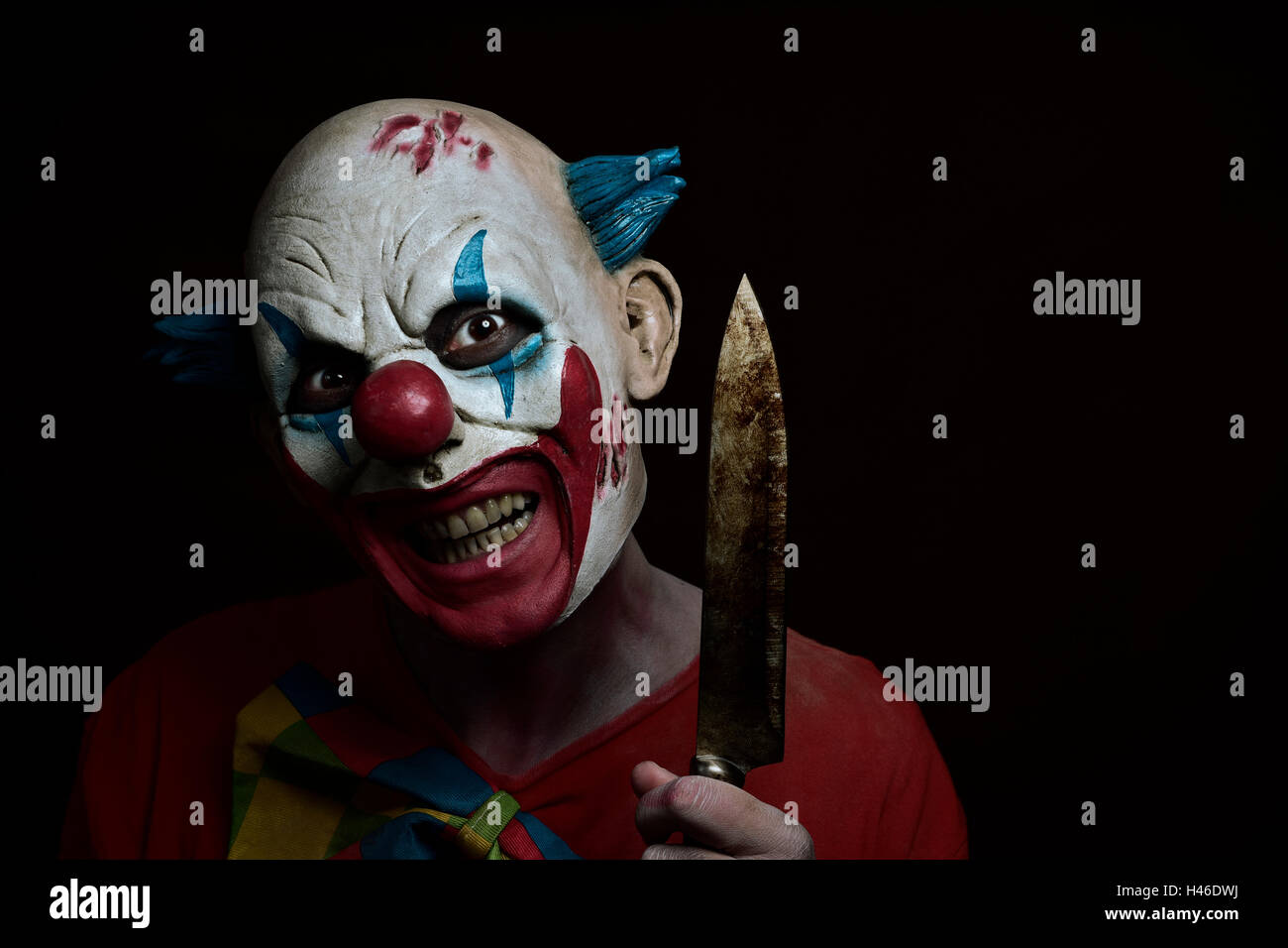 ein unheimlich böse Clown mit einem großen Messer in der Hand vor einem dunklen Hintergrund Stockfoto