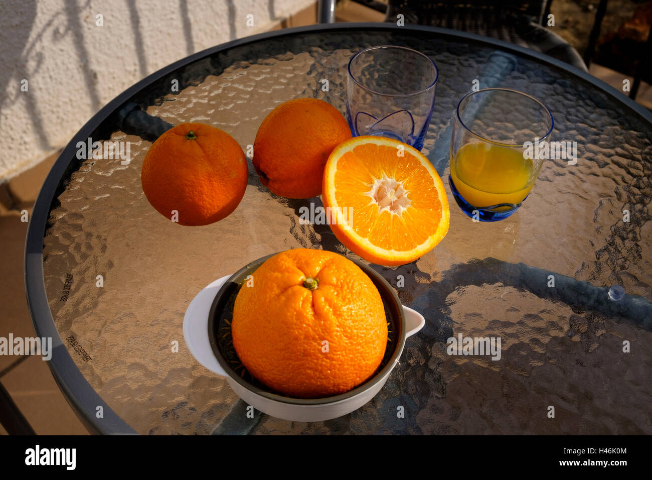 Orange Entsafter, Gläser und Schnitt orange auf einem Glastisch außerhalb ohne Menschen Stockfoto