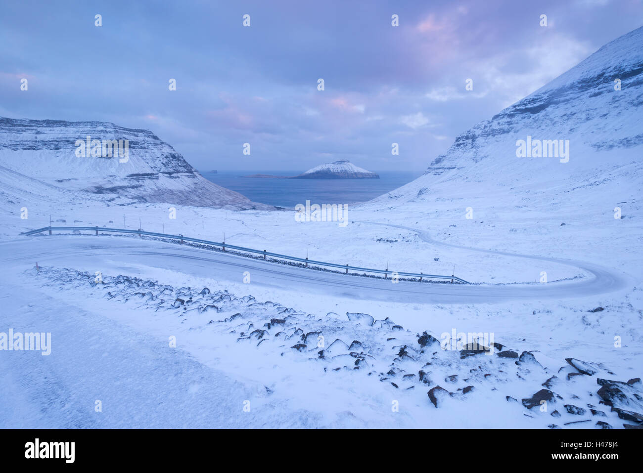 Schneebedeckte Straße schlängelt sich zwischen Bergen in der Nähe von Nordradalur auf der Insel Streymoy, Färöer Inseln, Dänemark, Europa. Gewinnen Stockfoto