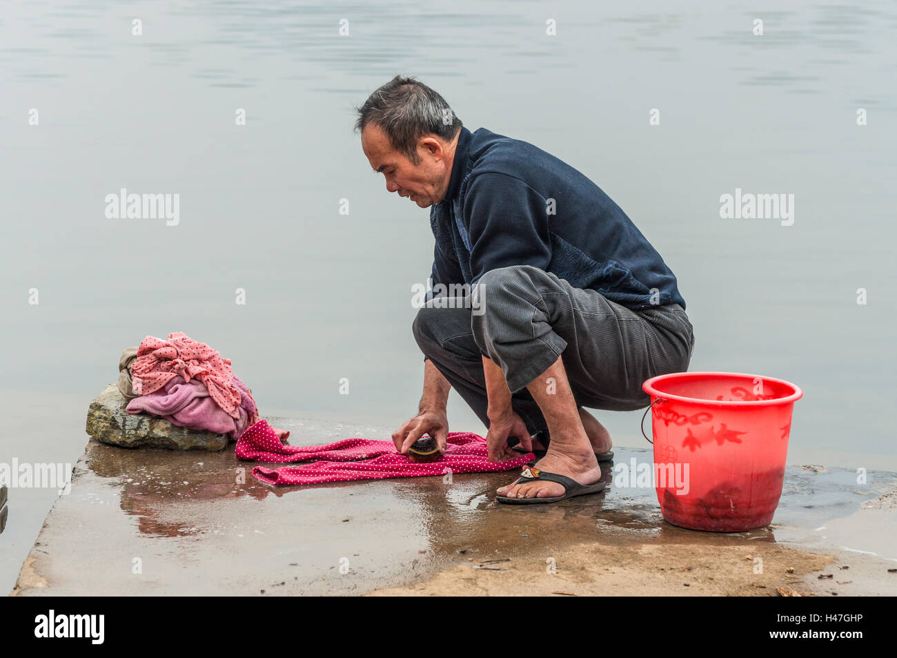 Dorf in China, im grünen, ländlichen asiatischen Bauernhof. Chinesische Bauern Mann seine Kleider waschen Stockfoto