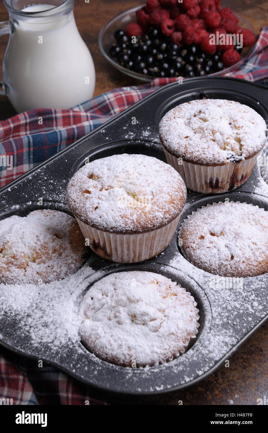Muffins Zucker Pulver in der Pfanne auf dem Tisch mit Karaffe Milch und Beeren Stockfoto