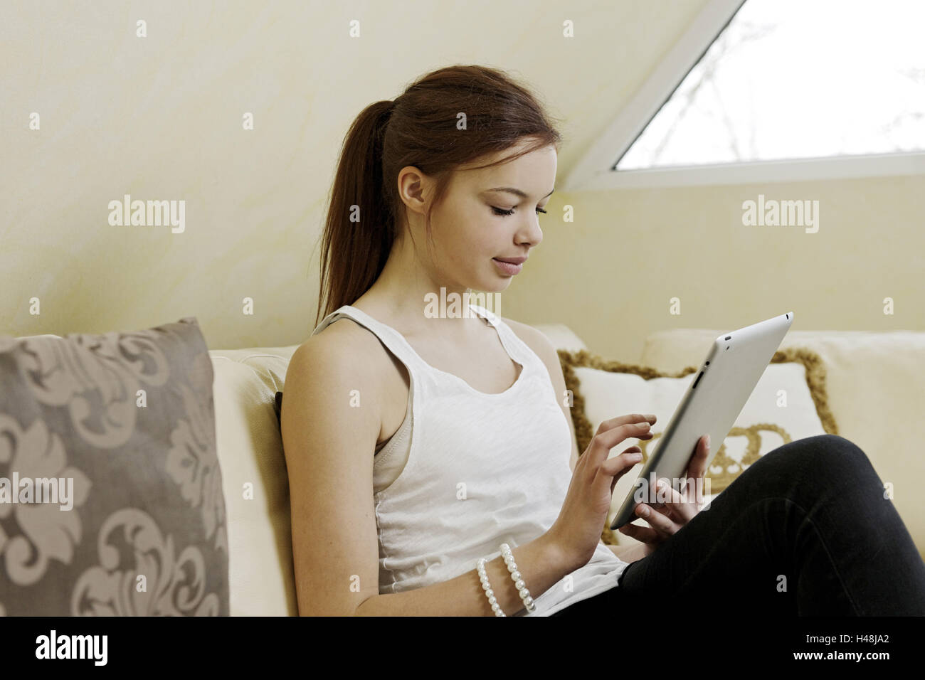 Teenager Mädchen sitzt mit Tabletcomputer auf Sofa, Porträt, Stockfoto