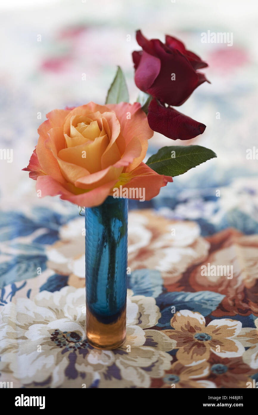 lachsfarben und rote Rose in blauem Glasvase auf Tabelle Kappen mit Floralem Design, Stockfoto
