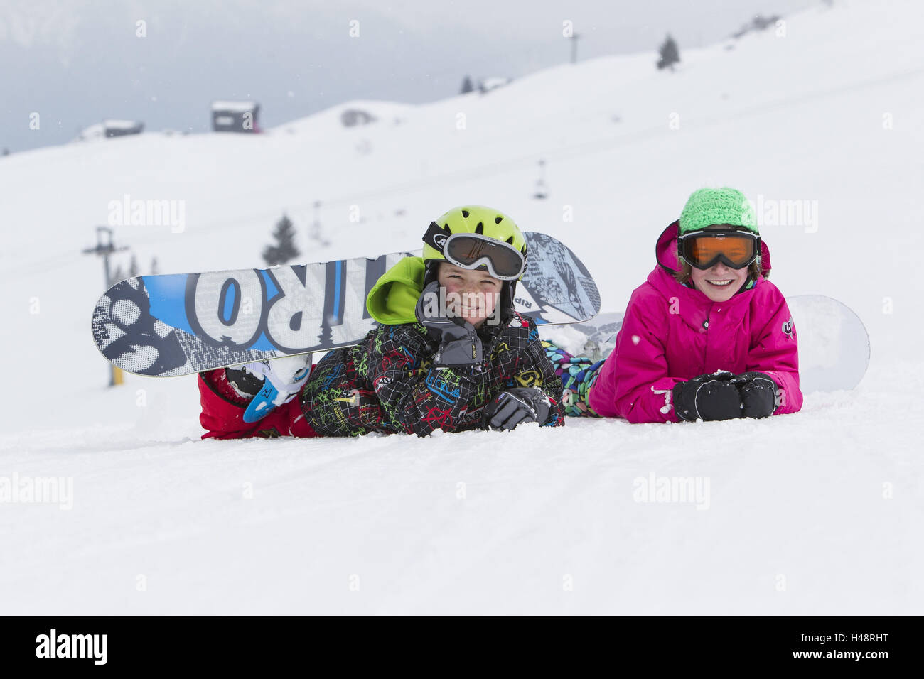 zwei Kinder liegen mit Snowboard im Schnee, lachen, Spaß, Rückfahrkamera, Stockfoto