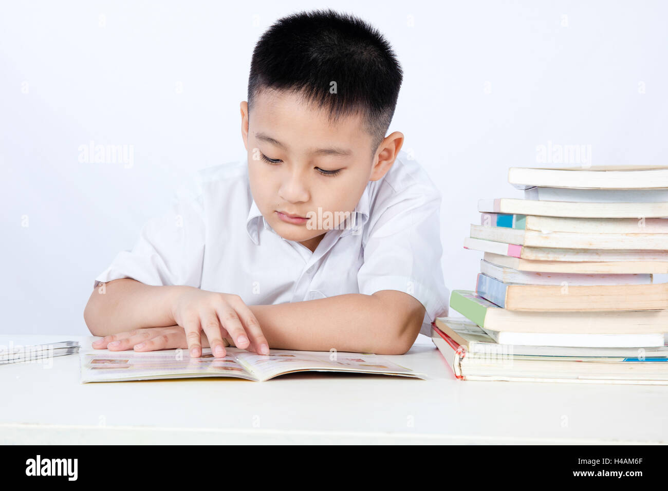 Asiatische chinesische Little Boy tragen Student einheitliche Lesung Lehrbuch in isolierten weißen Hintergrund. Stockfoto