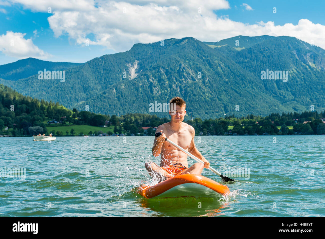Junger Mann sitzt auf einem Paddle Board auf See Schliersee, Upper Bavaria, Bavaria, Germany Stockfoto