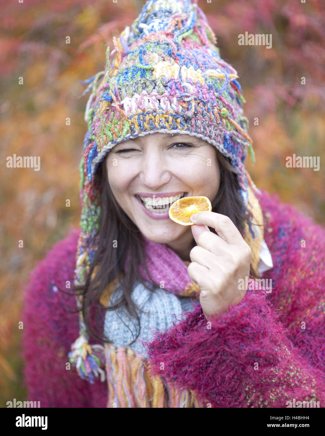 Frau mit Jacke, Mütze und Schal Holding Orangenscheibe in ihrer Hand, lachen, Portrait, Stockfoto