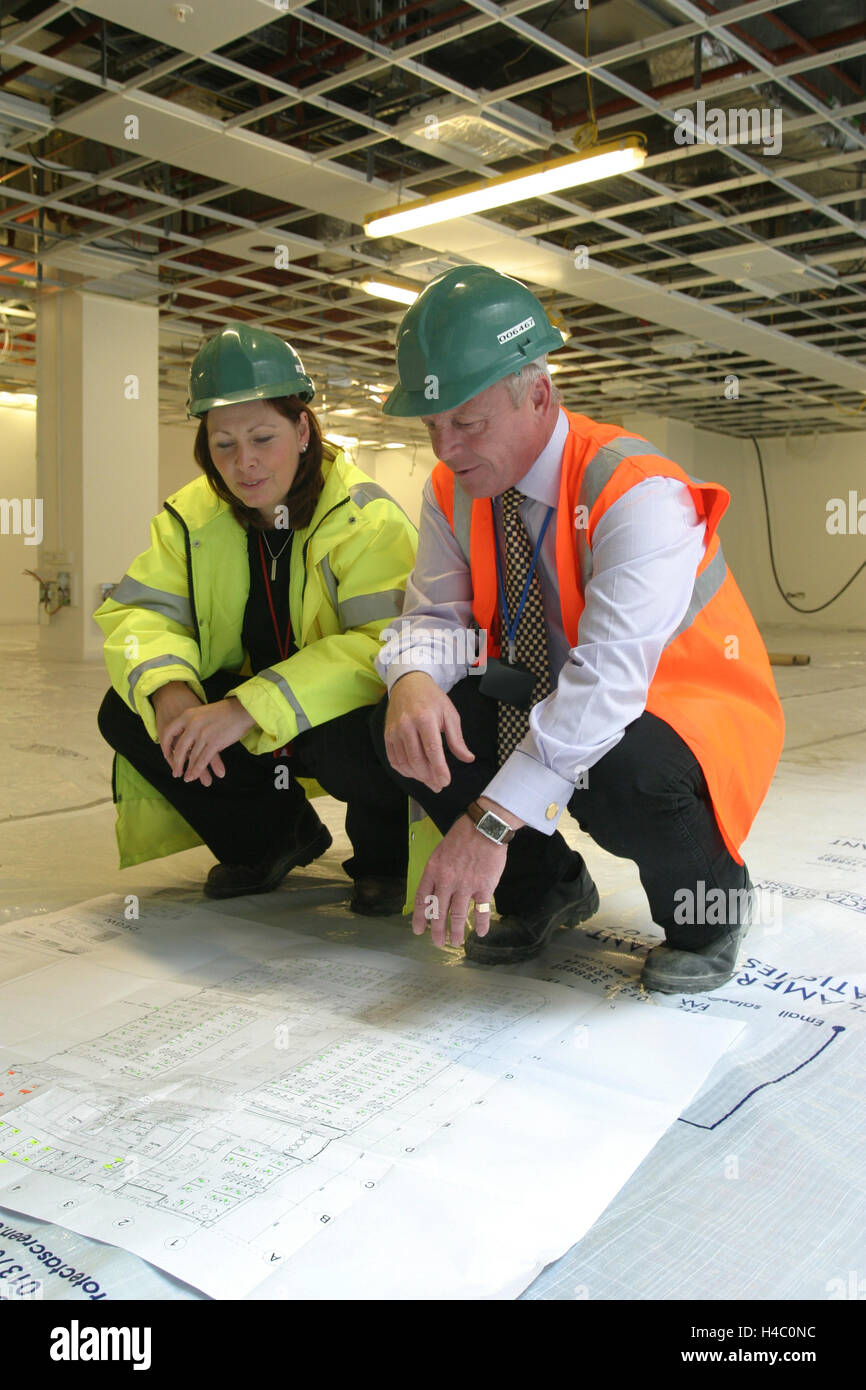 Männliche und weibliche Bauarbeiter untersuchen eine Konstruktionszeichnung in einem teilweise komplette Bürogebäude in central London, UK Stockfoto