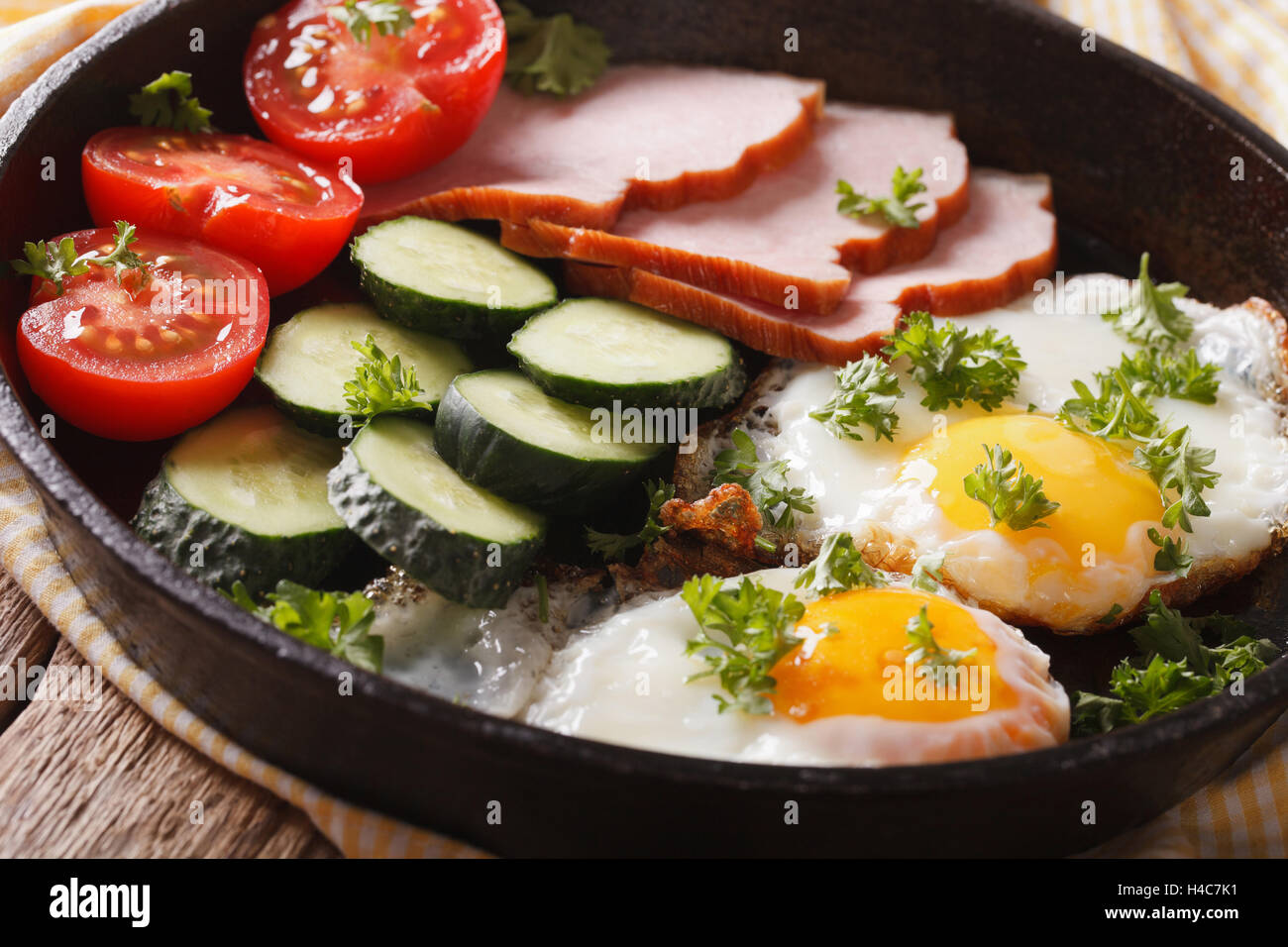 Hausgemachtes Frühstück: Spiegelei mit Schinken und frischem Gemüse in einer Pfanne Nahaufnahme. Horizontale Stockfoto