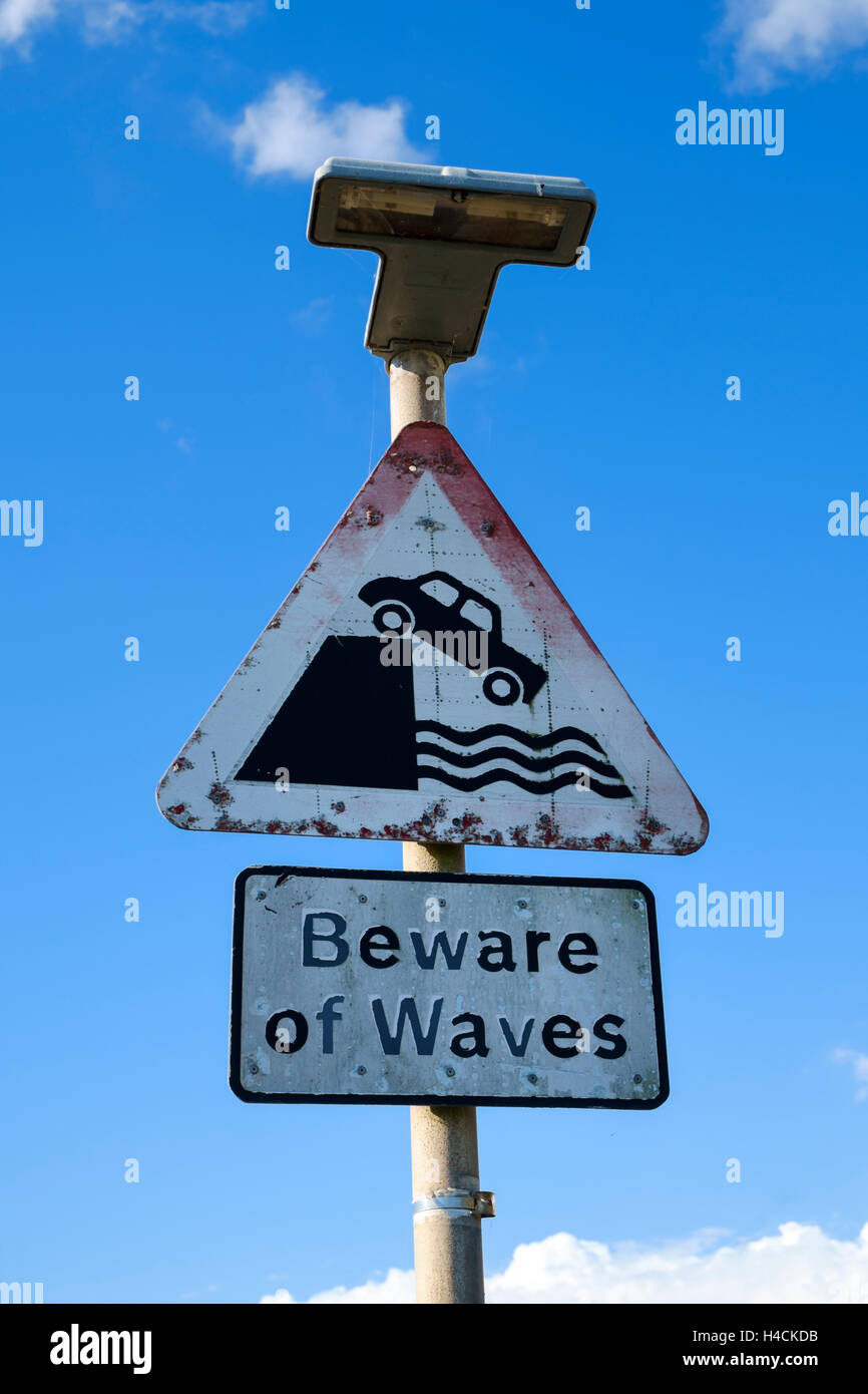 UK-Warnung Verkehrsschilder - Vorsicht bei Wellen auf der Straße vor uns im Hafen, zerfressen von Wellen Stockfoto