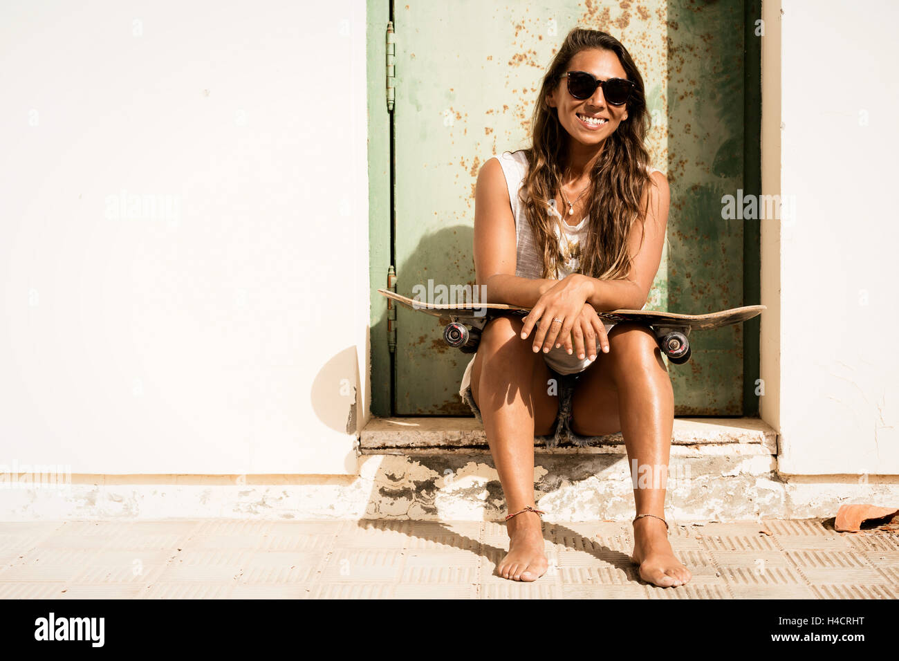 Mädchen mit einem Skateboard vor Grunge Tür sitzen. Stockfoto