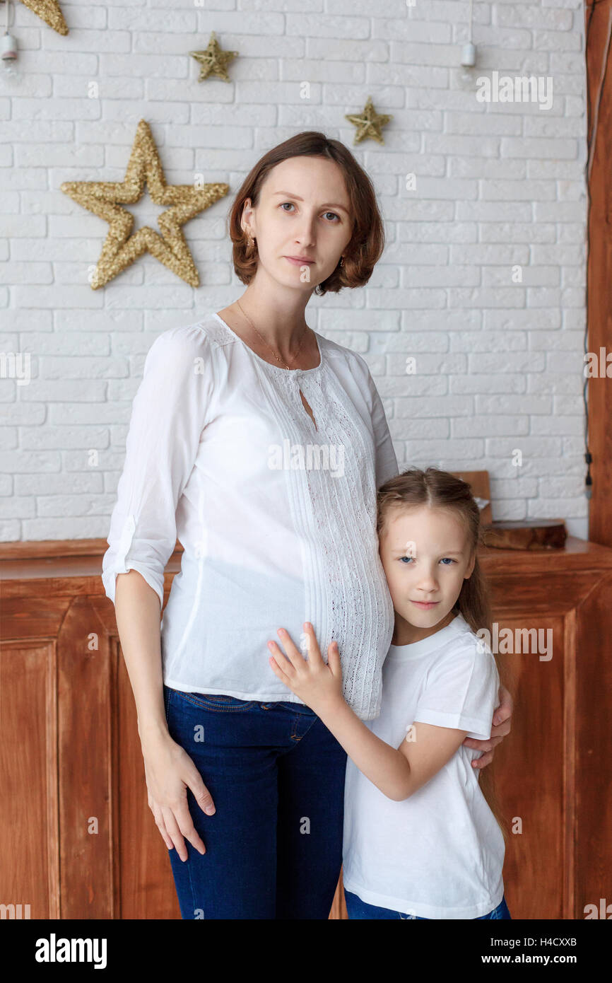 Niedliche kleine Mädchen umarmt ihre schwangere Mutter im studio Stockfoto