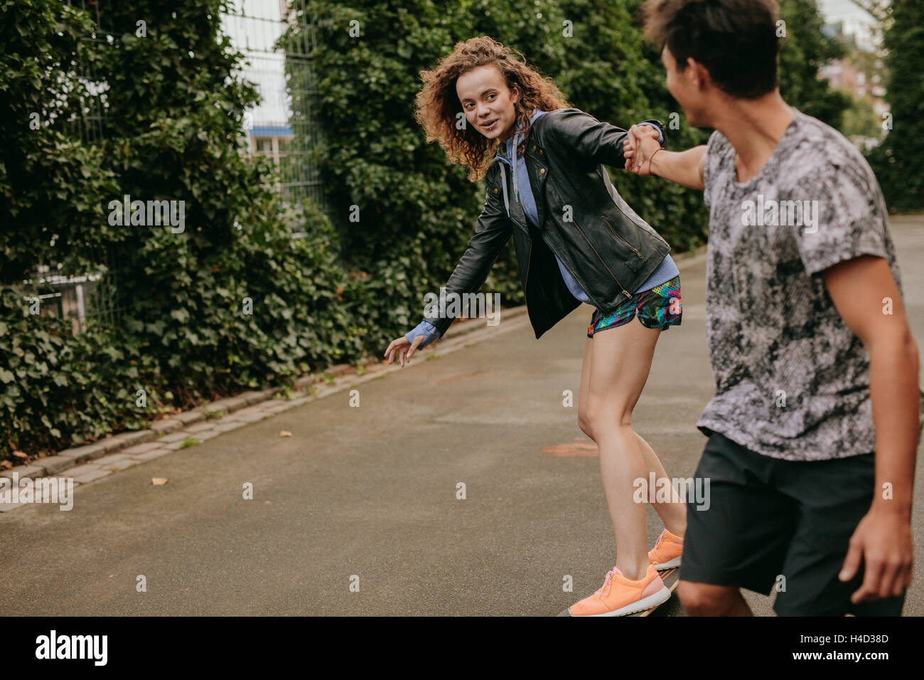 Teenager-Mädchen auf einem Skateboard mit Unterstützung von ihrem Freund. Frau auf einem Basketballfeld mit Freund Skaten. Stockfoto