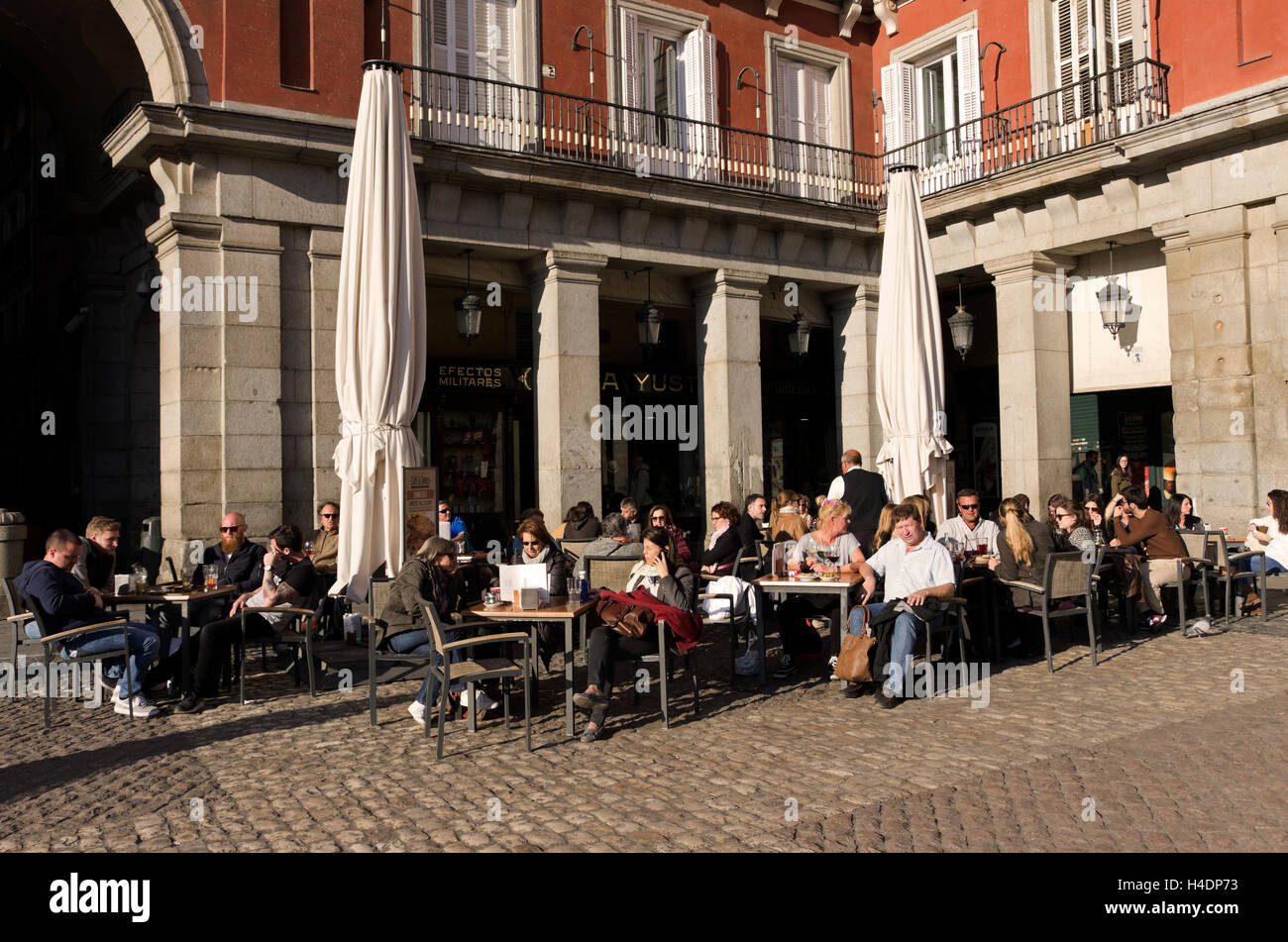 Plaza Mayor, Touristen und einheimischen Schluck Kaffee, Wein oder Bier, sitzen sie an Tischen in der Nachmittagssonne. farbige Gebäude auf der Rückseite Stockfoto