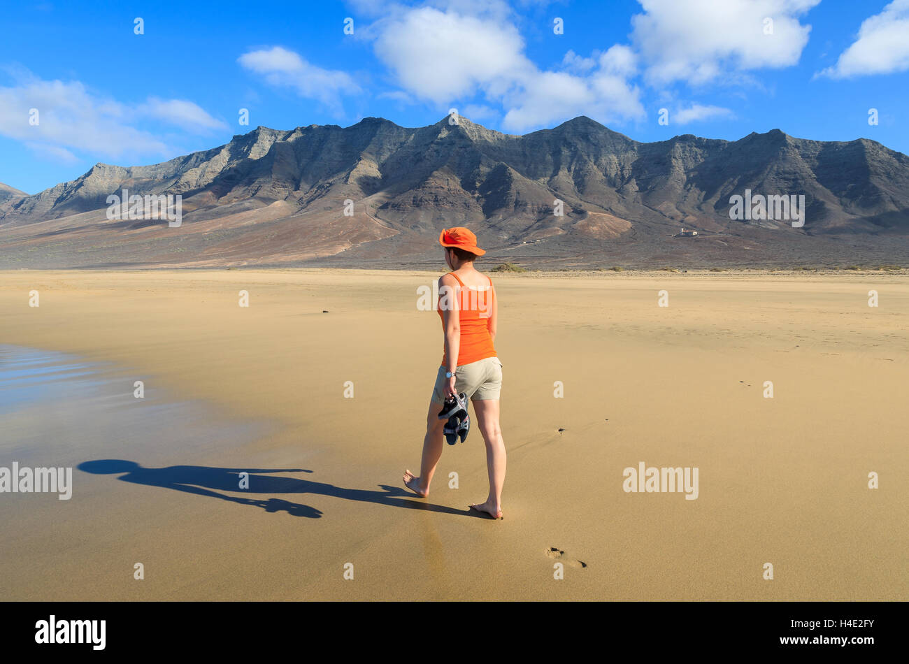 Junge Frau Tourist in rotem Hemd und Hut zu Fuß nass im goldenen Sand Cofete Strand, Fuerteventura, Kanarische Inseln, Spanien Stockfoto