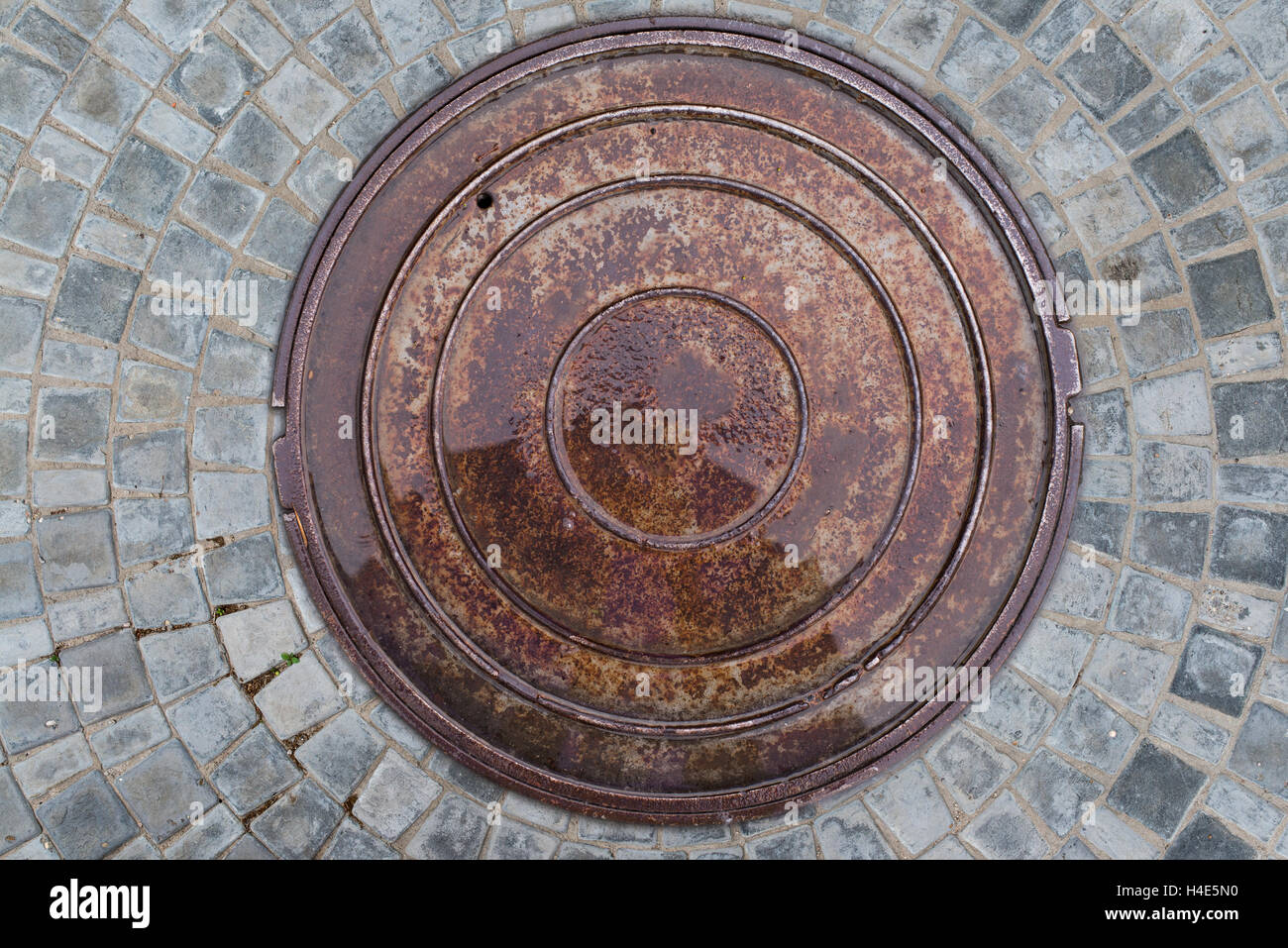 Nahaufnahme Foto von Rost alte Kanalisation Kanaldeckel auf der städtischen Asphaltstraße. Regen-Szene. Stockfoto