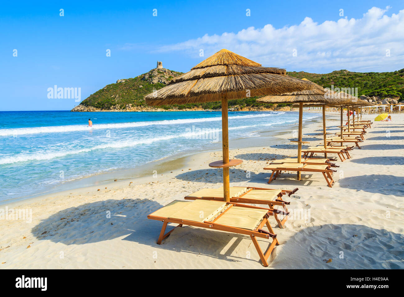 Liegestühle mit Sonnenschirmen am schönen Strand von Porto Giunco und unbekannter Mann Baden im Meer, Insel Sardinien, Italien Stockfoto