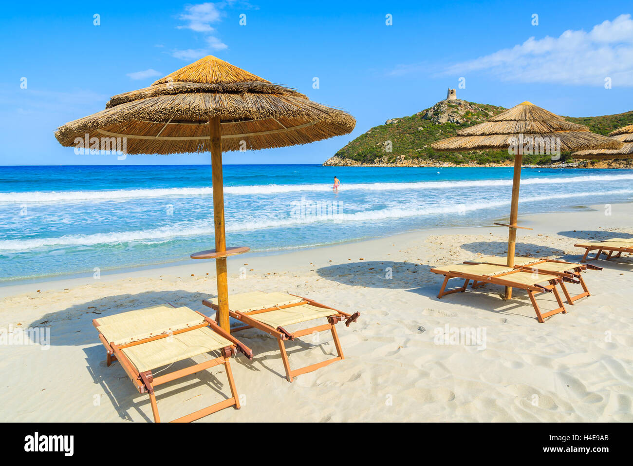 Liegestühle mit Sonnenschirmen am schönen Strand von Porto Giunco und unbekannter Mann Baden im Meer, Insel Sardinien, Italien Stockfoto