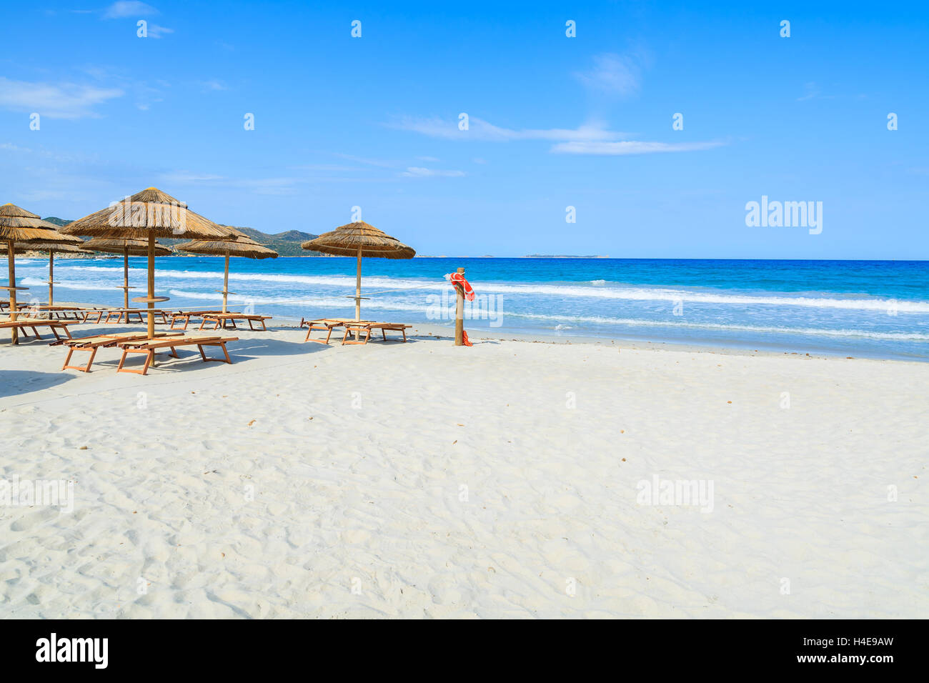 Liegestühle mit Sonnenschirmen und Lebensretter Ring am weißen Sandstrand in Porto Giunco Bucht, Insel Sardinien, Italien Stockfoto