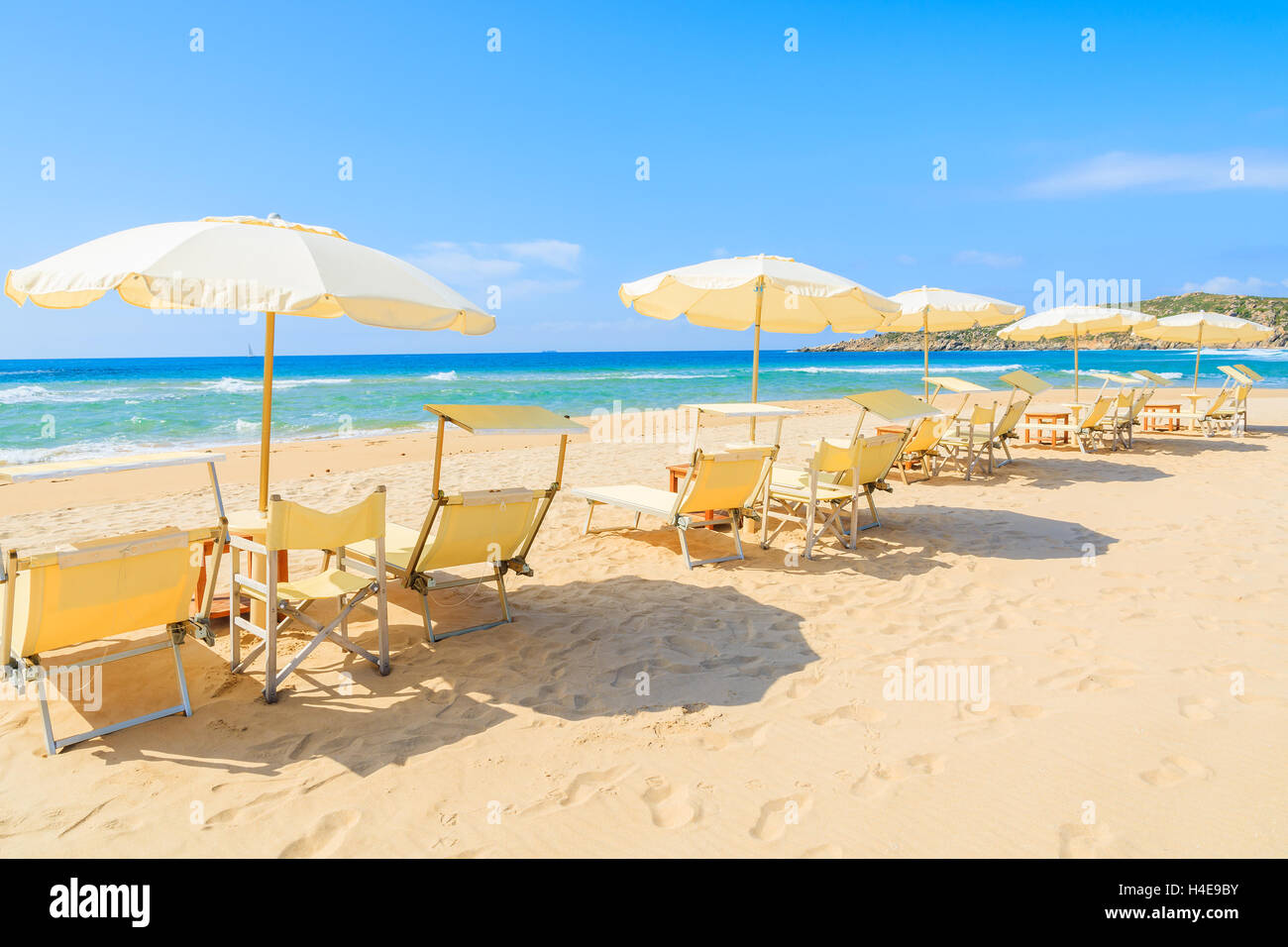 Liegestühle mit Sonnenschirmen auf Sand und Blick auf türkisfarbenes Meerwasser, Sa Colonia, Insel Sardinien, Italien Stockfoto