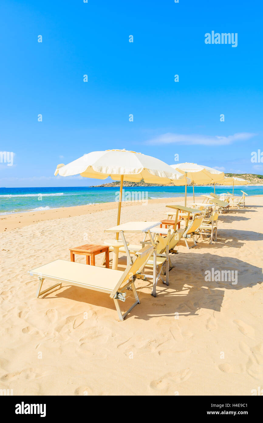 Liegestühle mit Sonnenschirmen auf Sand und Blick auf türkisfarbenes Meerwasser, Sa Colonia, Insel Sardinien, Italien Stockfoto