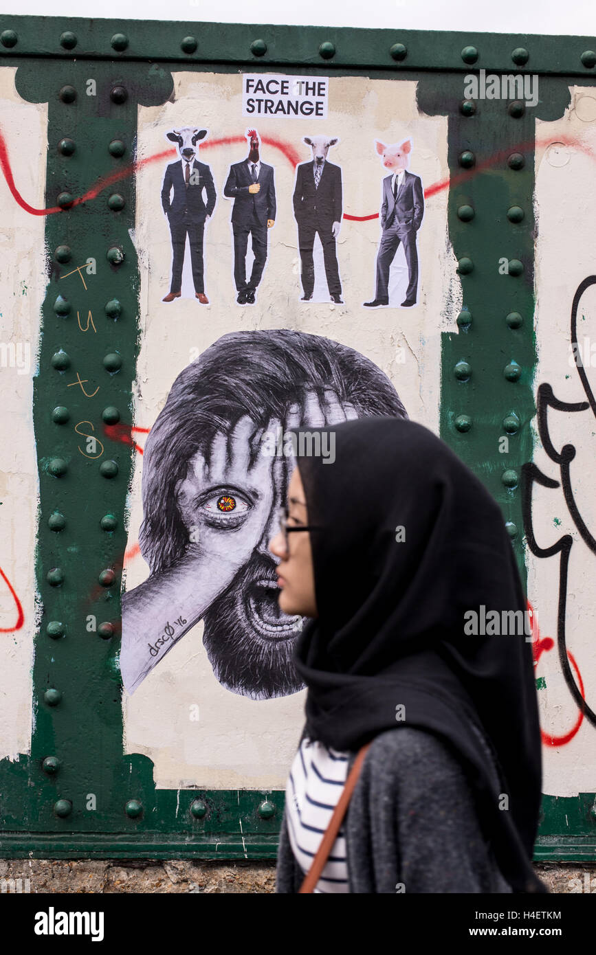 Muslimische Frau trägt einen traditionellen schwarzen Hijab oder Schleier zu Fuß vor einer Wand mit Wandbild in Brick lane Stockfoto