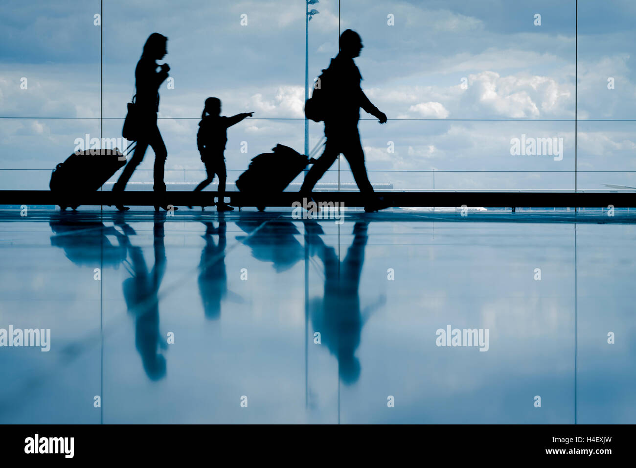 Silhouette der jungen Familie mit Gepäck zu Fuß am Flughafen, Mädchen am Fenster zeigen Stockfoto