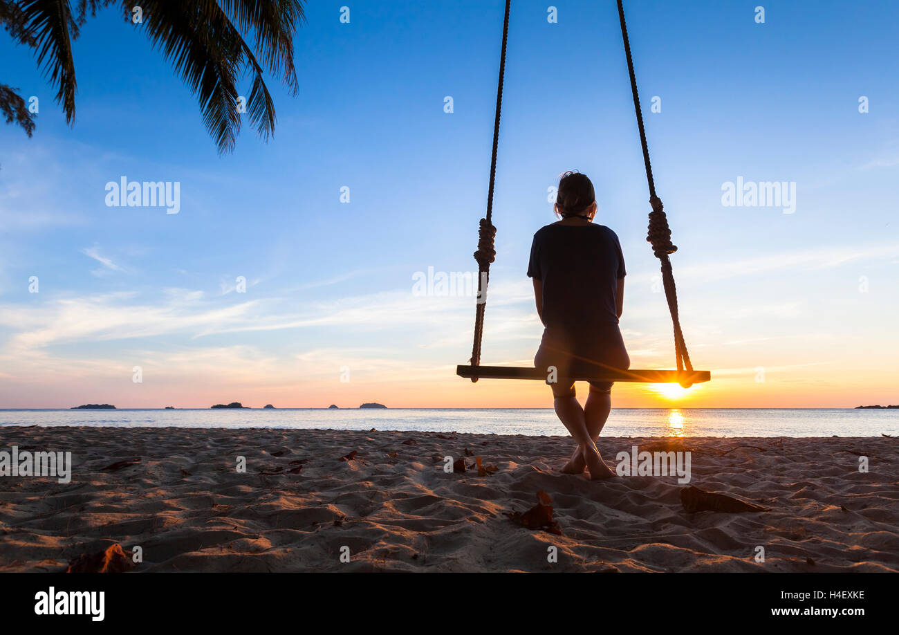 Einsame Frau sitzt auf einem Seil schwingen bei Sonnenuntergang am Meer und denken über das Leben Stockfoto