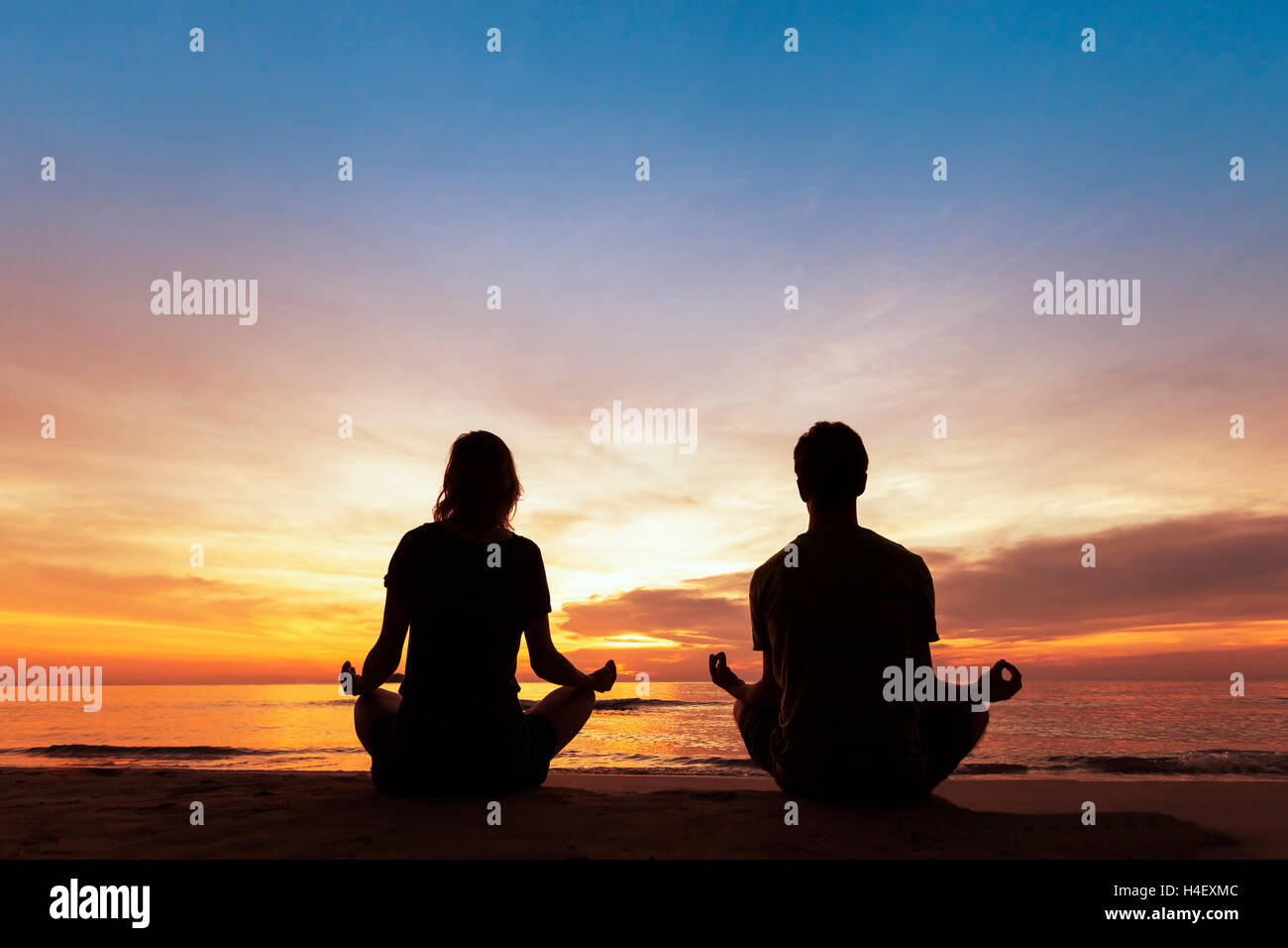 Zwei Menschen praktizieren Yoga am Strand bei Sonnenuntergang für gesunden Lebensstil Stockfoto