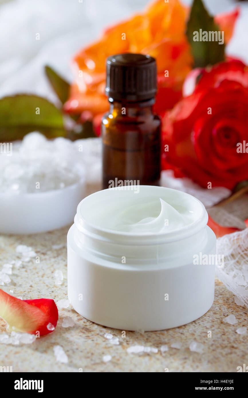 Gesichtscreme mit Rosen, Flasche Aromatherapie ätherische Öl und Salz auf braunen Stein Hintergrund. Rose Spa. Stockfoto
