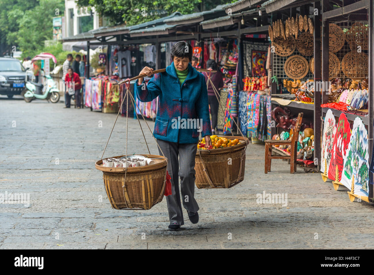 Chinesische Frau trägt Körbe mit Produkten und Obst auf dem lokalen Markt in Yangshuo, China zu verkaufen Stockfoto