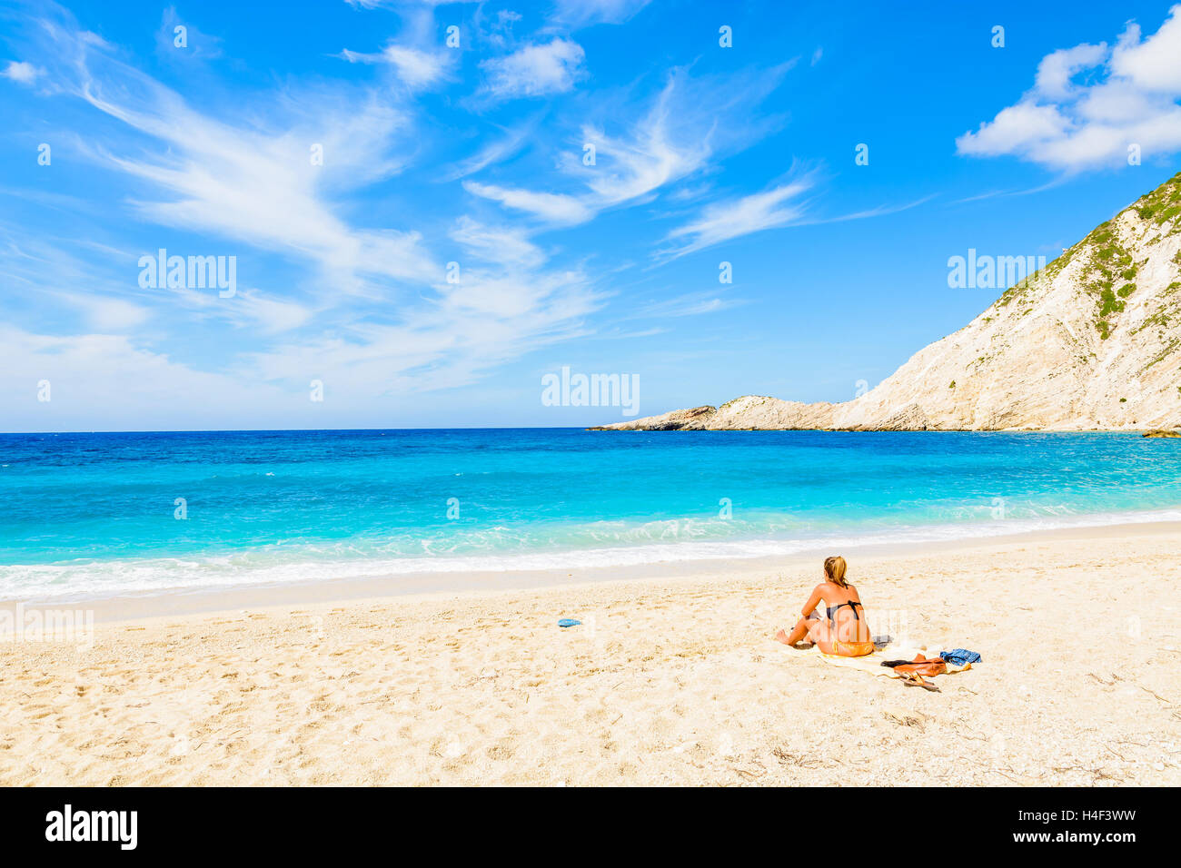 Nicht identifizierte junge attraktive Frau sitzen auf Sandstrand und azurblaues Meer mit Meerblick im Petani Bucht, Insel Kefalonia, Griechenland Stockfoto