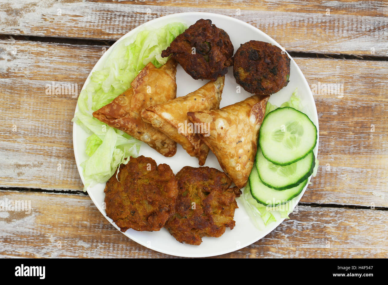Teller voll mit indischen snacks einschließlich Zwiebel-Bhajis, Samosas und Pakoras auf rustikalen Holzoberfläche Stockfoto