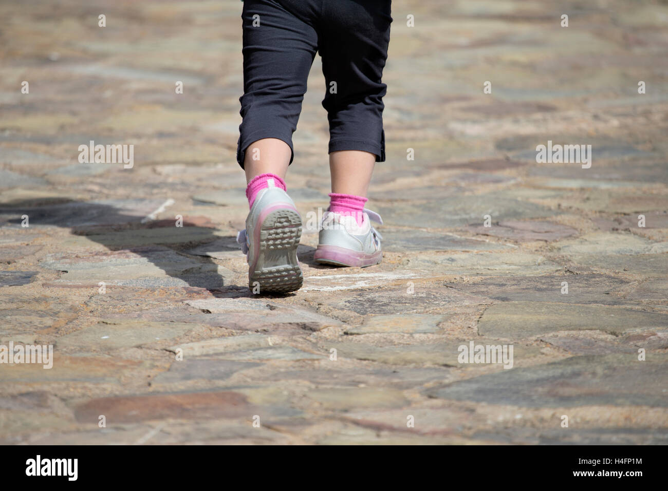 Nahaufnahme von unerkennbar kleinen Mädchen in Turnschuhen laufen auf Stein gemahlen im Sonnenlicht Stockfoto