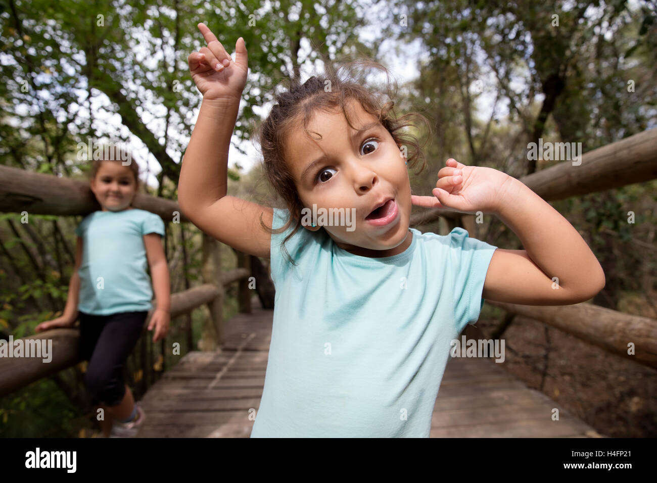 Porträt von fröhlichen kleinen Mädchen gestikulieren und machen lustige Grimasse in die Kamera im Park. Ihre Schwester auf Hintergrund. Stockfoto