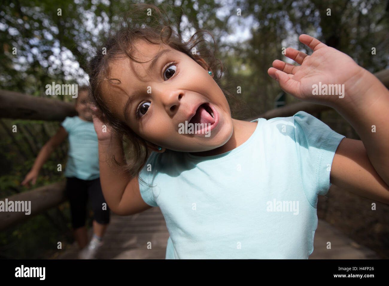 Porträt von fröhlichen kleinen Mädchen gestikulieren und machen lustige Grimasse in die Kamera im Park. Ihre Schwester auf Hintergrund. Stockfoto