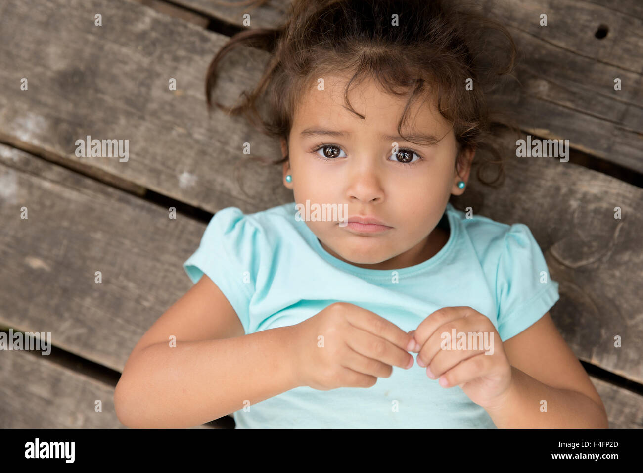 Draufsicht der niedliche kleine Mädchen mit dem lockigen Haar, Blick in die Kamera mit unglücklichen Gesicht über hölzerne Boden. Stockfoto