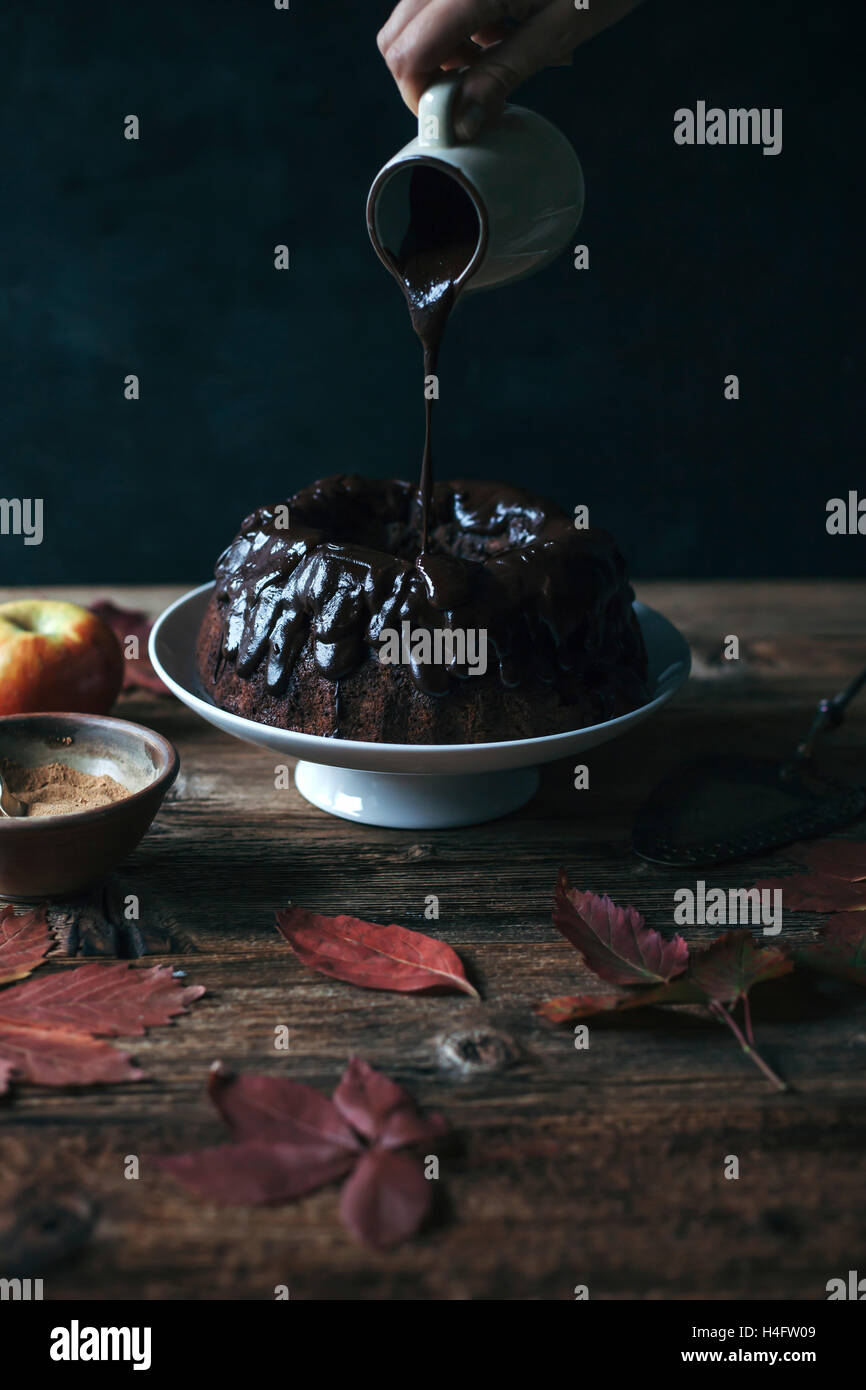 Johannisbrot und Apple Bundt Kuchen auf eine Kuchenplatte und weibliche Hand nieselt Schokoladen ganache Stockfoto