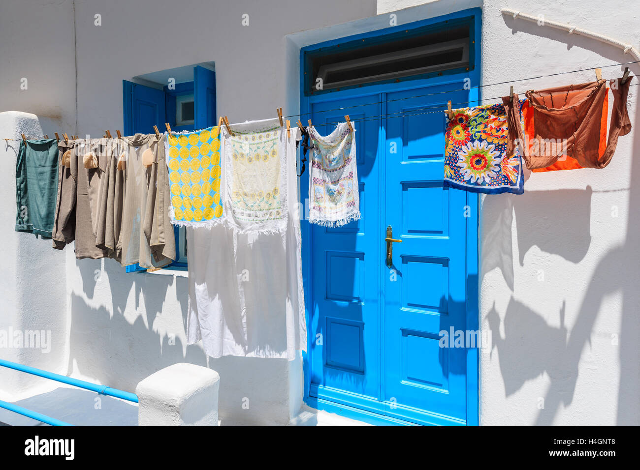 Klamotten, die vor einem Haus mit blauen Türen und Fenster auf weiß getünchten Straße in die Stadt Mykonos, Kykladen, Griechenland Stockfoto