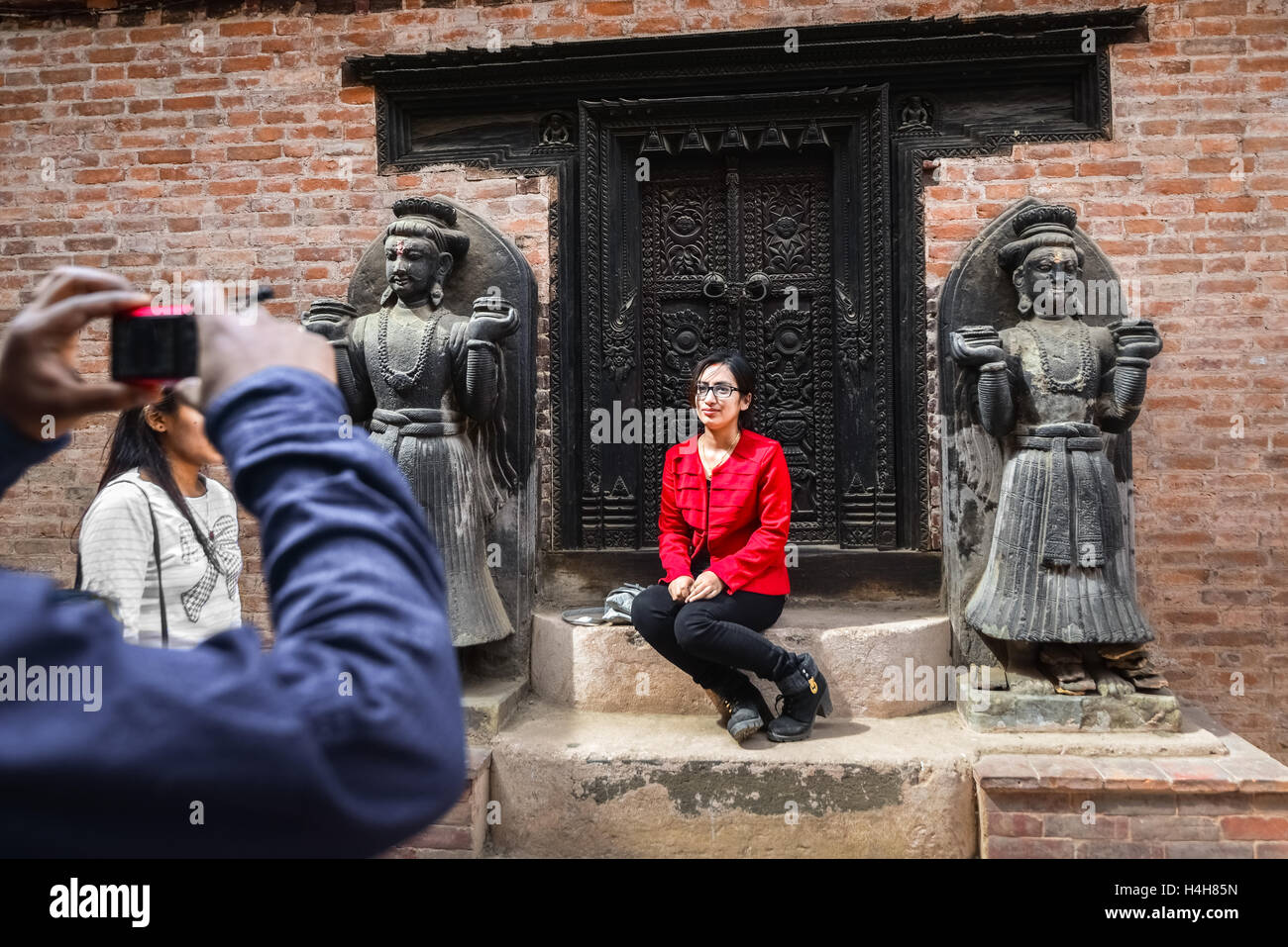 Ein Besucher posiert für ein Foto vor einer Tür am Palast der 'fünfundfünfzig Fenster' in Bhaktapur. Durbar Square, Bhaktapur, Bagmati, Nepal. Stockfoto