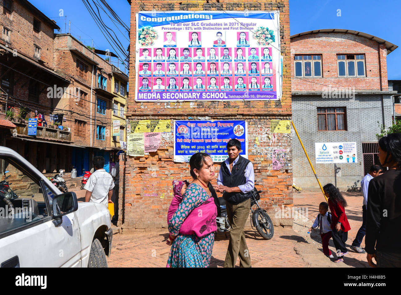 Menschen, die vor einem Schulgebäude mit Abschlussplakat in der Mitte des Wohngebiets in Bhaktapur, Nepal, stehen. Stockfoto