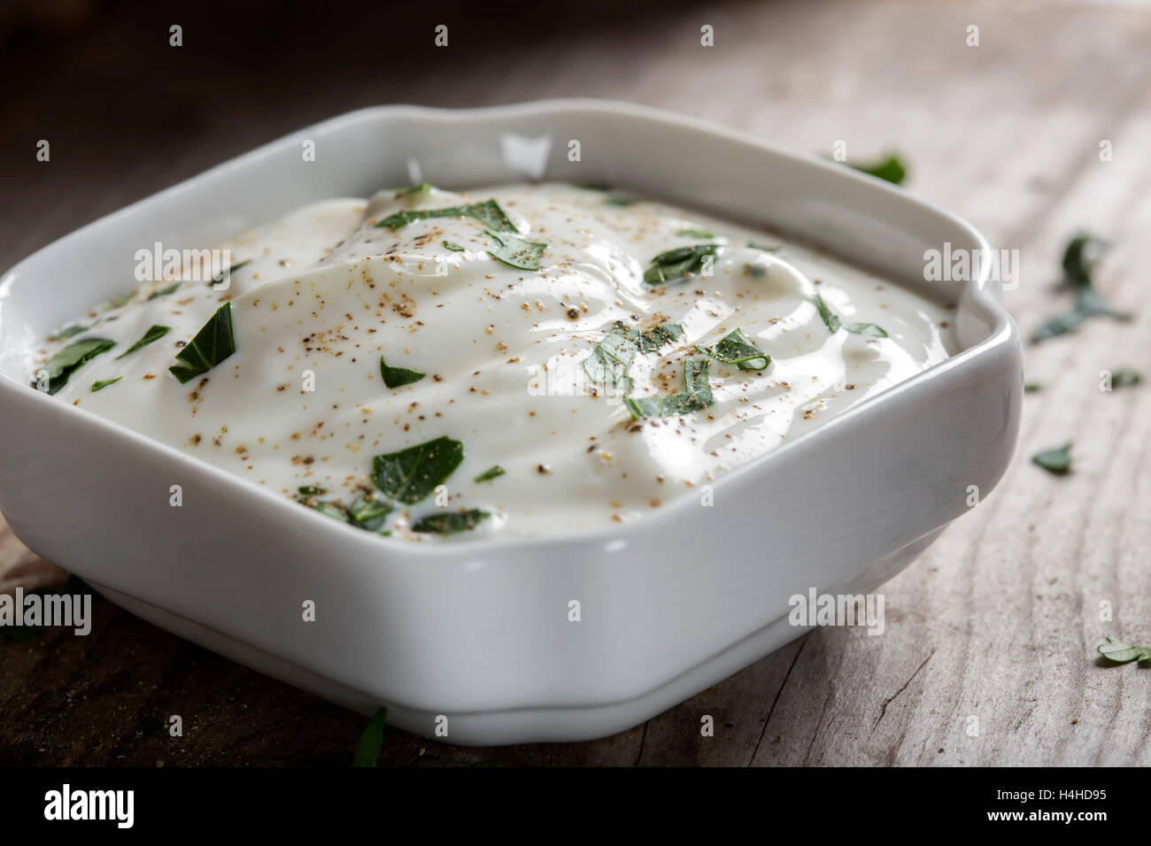 Saure Sahne oder Joghurt mit Kräutern und Pfeffer in weiße Schüssel auf hölzernen Hintergrund hautnah Stockfoto