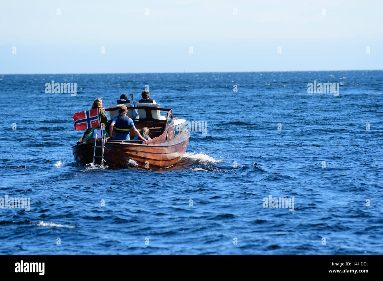 Kleines Boot mit norwegischer Flagge und eine Familie auf dem ruhigen Meer in Südnorwegen Stockfoto