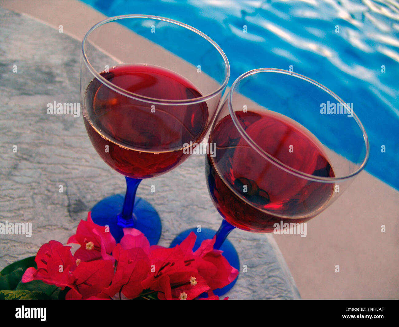 Rosenweingläser auf der Terrasse im Freien am Ferienschwimmbad bei Sonnenuntergang mit Blumen Stockfoto