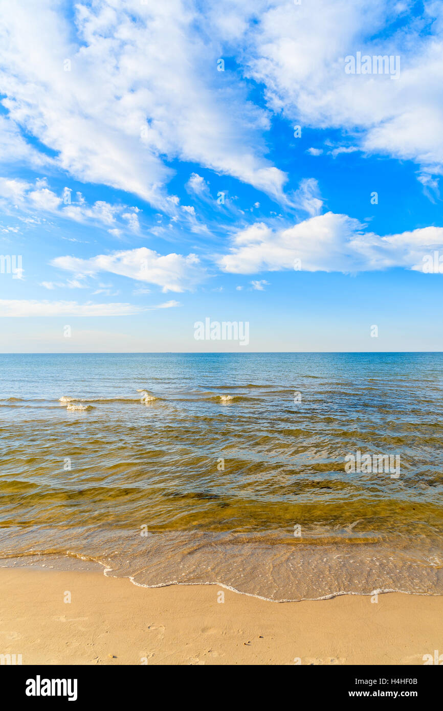 Wellen des Meeres auf Sandstrand und weißen sonnigen Wolken am blauen Himmel in Debki Dorf, Ostsee, Polen Stockfoto